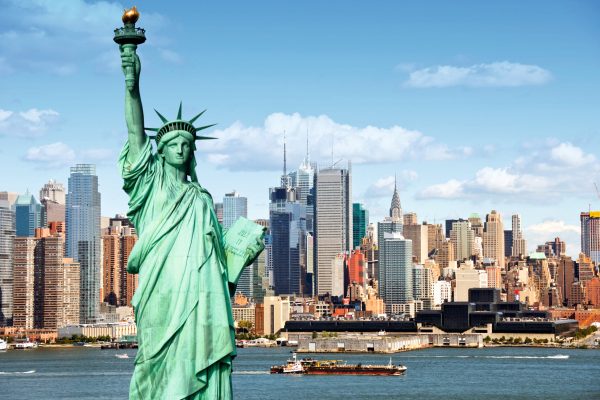 TRAVEL - NEWS - SUNDAY 17 OCTOBER 2021 - UNDER EMBARGO: MARELLA CRUISES TO ADD SHIP NUMBER FIVE TO FLEET AND SAILS TO THE STATES IN 2023:   new york city skyline cityscape with statue of liberty over hudson river. with midtown Manhattan skyscrapers and freight sailing ship in usa america.